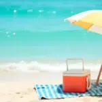 Back to beach essentials image of an umbrella and cooler on the beach.